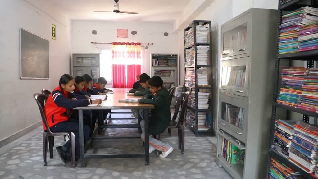 Students reading at a table in the library, between tall bookshelves